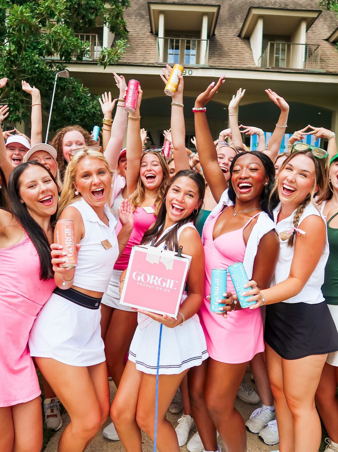 Alpha Delta Pi members cheering with GORGIE energy drink cans in front of the chapter house
