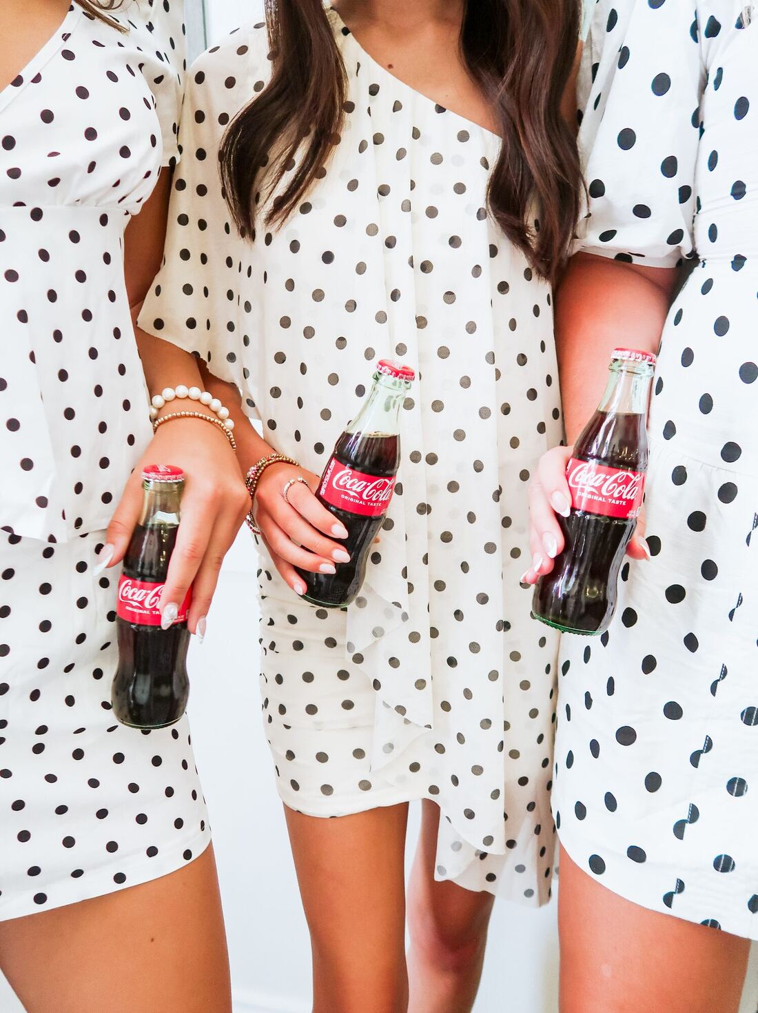 Three members in matching polka-dot dresses holding glass Coca-Cola bottles